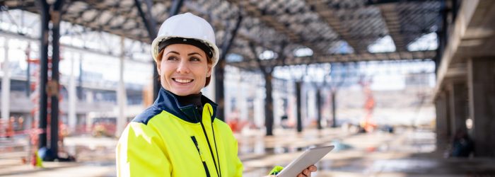 A woman engineer with tablet standing on construction site, working. Copy space.